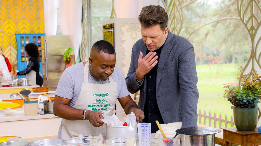 Pimpolho e Carlos Bertolazzi em frente a bancada, no episódio de estreia do Bake Off Celebridades