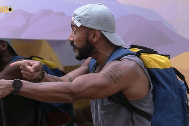 Ricardo exaltado, com as malas nas costas e apontando para o lado, no quarto deserto do BBB 23