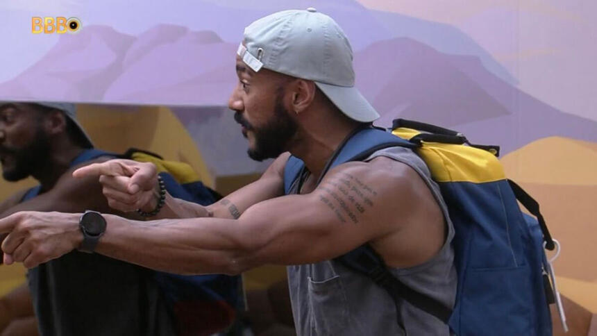 Ricardo exaltado, com as malas nas costas e apontando para o lado, no quarto deserto do BBB 23