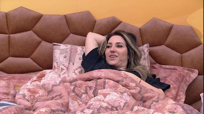 Amanda deitada na cama do Quarto Deserto, com camisa preta e mão na cabeça