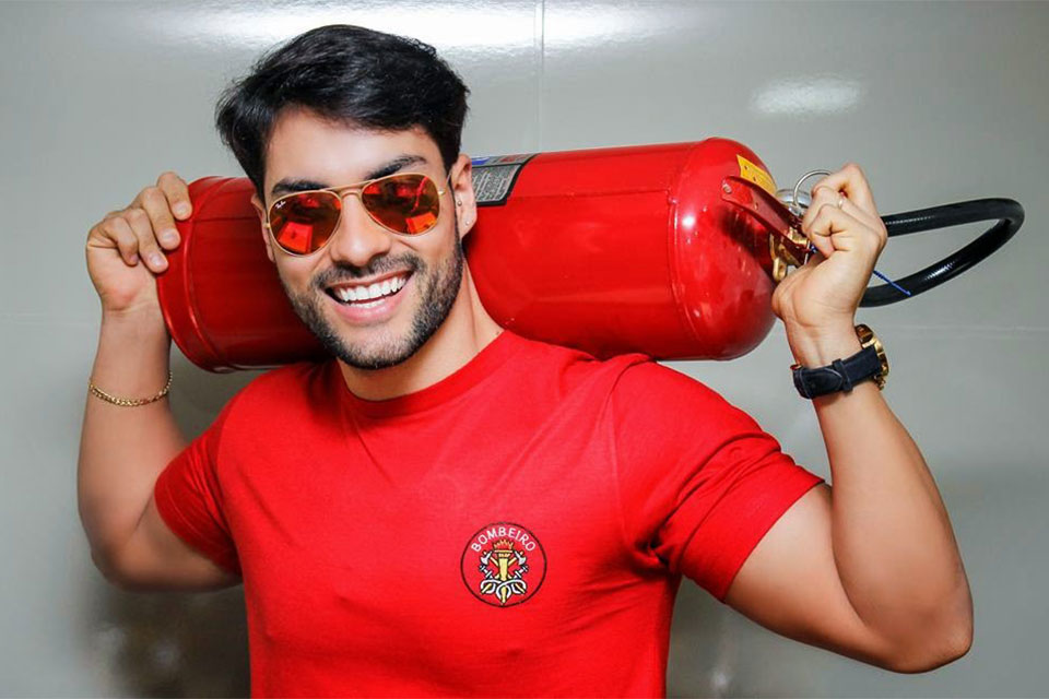Bruno Camargo com camisa vermelha segurando um extintor com as duas mãos durante ensaio fotográfico
