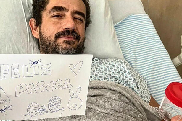 Felipe Andreoli deitado em uma cama de hospital, segundo uma folha escrito "Feliz Páscoa" e um potinho com as pedras retiradas do seu rim