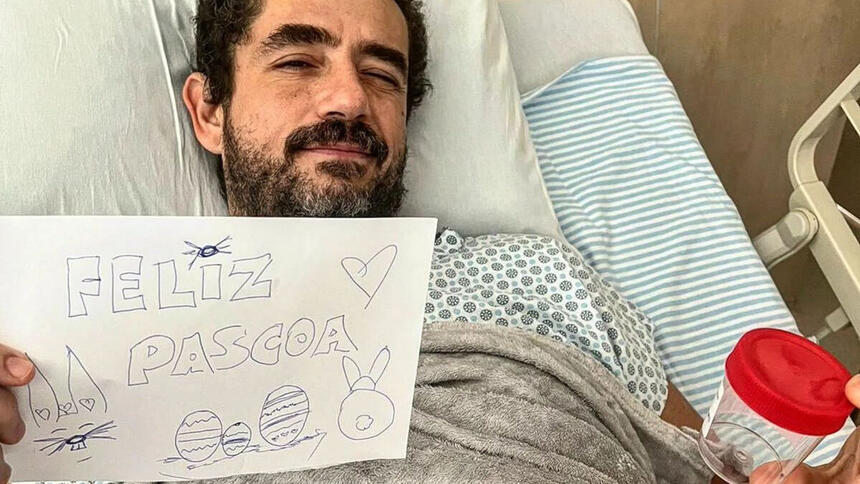 Felipe Andreoli deitado em uma cama de hospital, segundo uma folha escrito "Feliz Páscoa" e um potinho com as pedras retiradas do seu rim