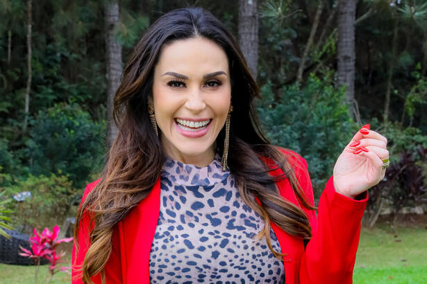 Nadja Haddad, utilziando uma roupa com tons vermelho, no jardim da tenda do Bake Off Celebridades