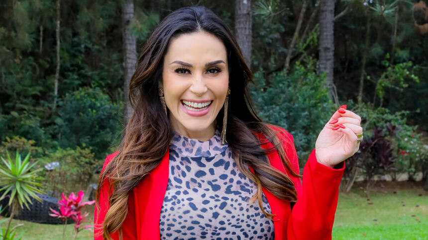 Nadja Haddad, utilziando uma roupa com tons vermelho, no jardim da tenda do Bake Off Celebridades