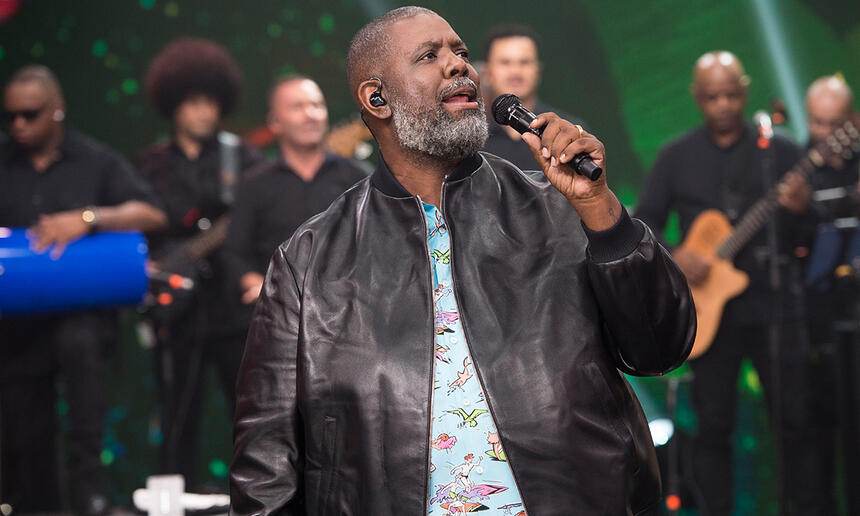 Péricles de jaqueta de couro e camisa azul, segudando o microfone durante gravação do Faustão na Band