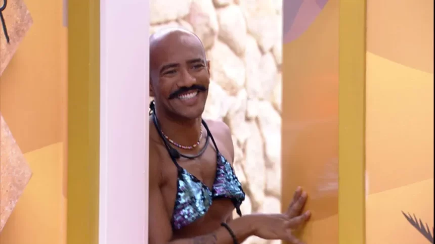 Ricardo sorrindo usando um biquini azul de Marvvila encostado na porta do Quarto Deserto