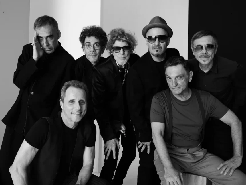 Arnaldo Antunes, Branco Mello, Paulo Miklos, Sérgio Britto, Nando Reis, Tony Bellotto e Charles Gavin sorrindo, durante sessão fotográfica em estúdio