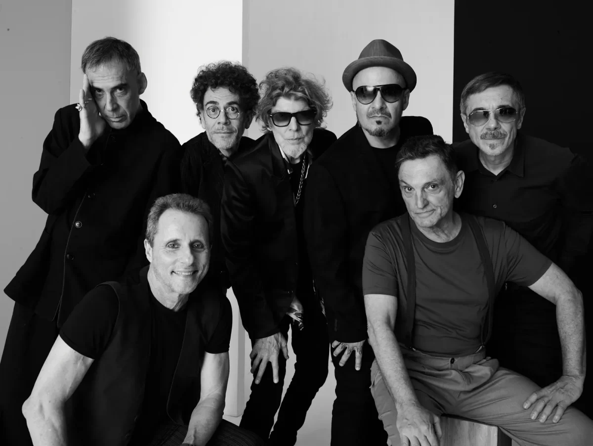 Arnaldo Antunes, Branco Mello, Paulo Miklos, Sérgio Britto, Nando Reis, Tony Bellotto e Charles Gavin sorrindo, durante sessão fotográfica em estúdio