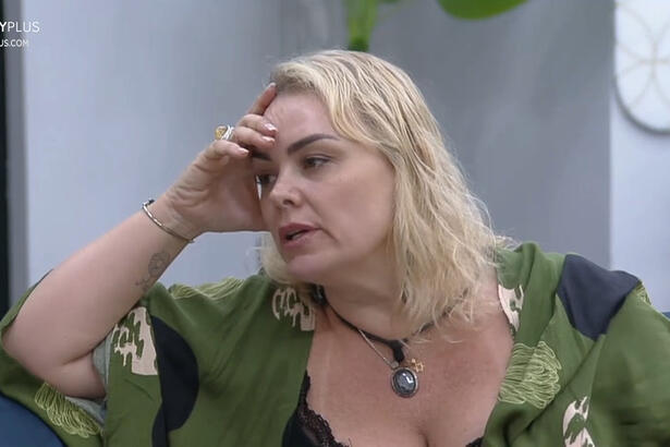 Ana Paula com a mão na cabeça, de camisa verde, com semblante preocupado, cabelo solto