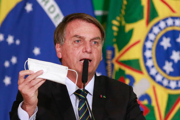 Bolsonaro segurando uma máscara e falando no microfone