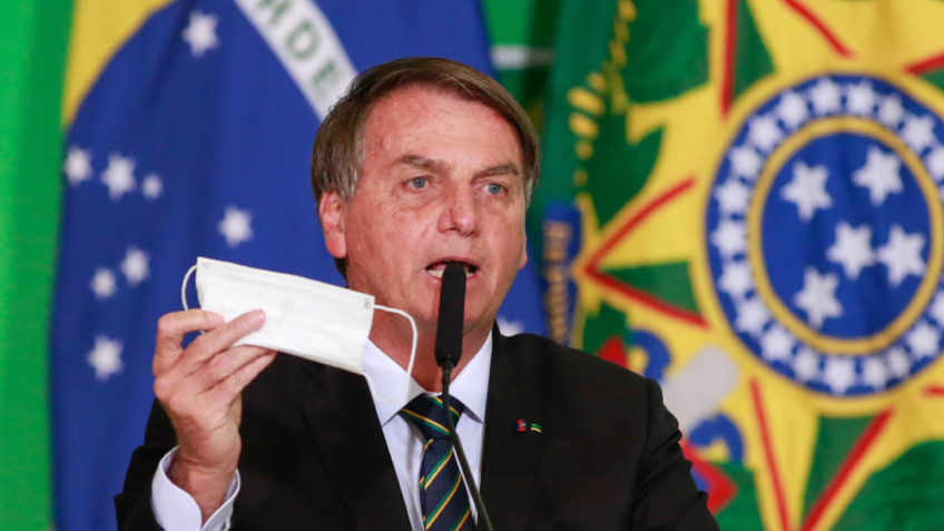 Bolsonaro segurando uma máscara e falando no microfone