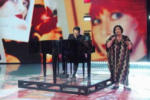 Déa Lúcia se apresentando no palco do Domingão, ao lado de um pianista, em homenagem a Rita Lee