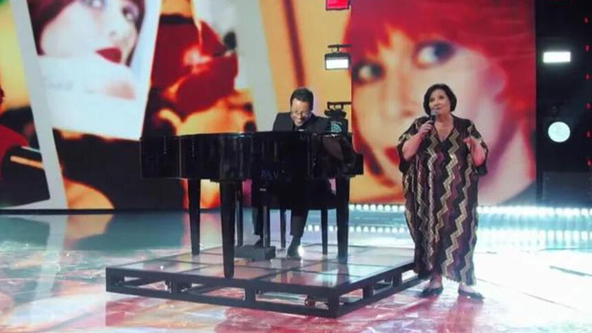 Déa Lúcia se apresentando no palco do Domingão, ao lado de um pianista, em homenagem a Rita Lee