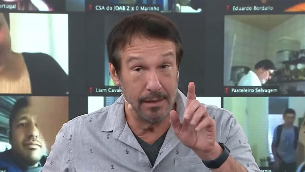 Emílio Surita de camisa polo cinza, sentado durante apresentação de programa na Jovem Pan
