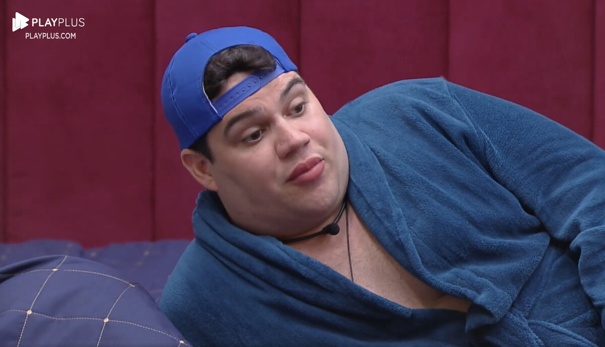 Erick de boné e toalha azul deitado na cama do A Grande Conquista
