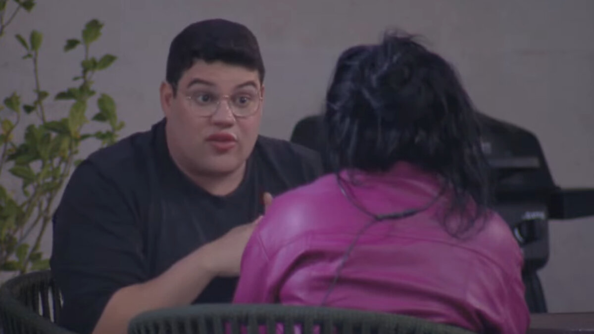 Erick Ricarte (de frente) e Janielle Nogueira (de costas para a câmera) conversando sentados, na área externa do A Grande Conquista