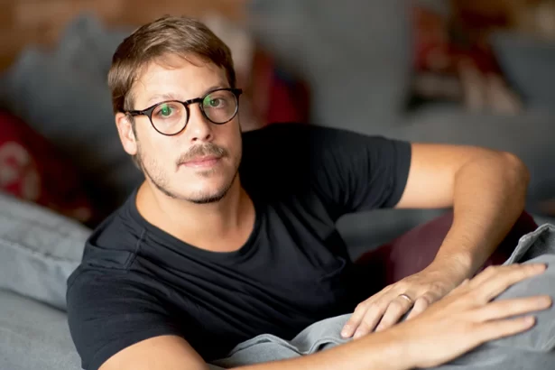 Fábio Porchat deitado numa rede, de camisa preta e óculo de grau, com semblante sério, durante ensaio fotográfico