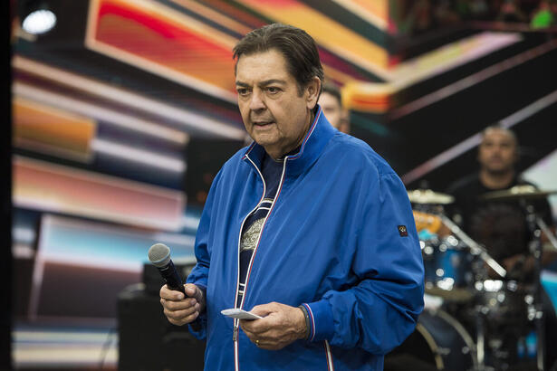 Faustão olha para o chão do cenário da Band enquanto segura um microfone