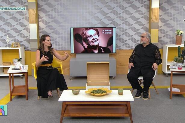 Apresentadora Regiane Tápias e Leão Lobo no cenário da TV Gazeta em São Paulo. Ao fundo uma TV com a imagem de Palmirinha