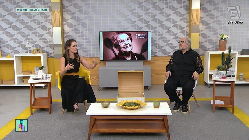 Apresentadora Regiane Tápias e Leão Lobo no cenário da TV Gazeta em São Paulo. Ao fundo uma TV com a imagem de Palmirinha