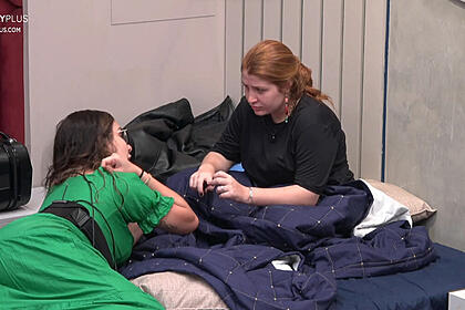 Giulia Garcia de camisa preta sentada na cama em frente a Stephanie Gomes de vestido verde, cabelo solto, molhado, deitada na cama