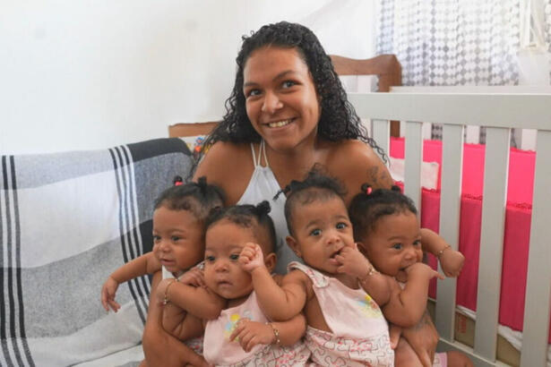 Mãe segurando as quadrigêmeas sentada em um sofá, em trecho do Globo Repórter