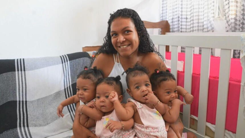 Mãe segurando as quadrigêmeas sentada em um sofá, em trecho do Globo Repórter