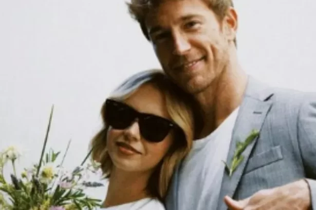 Isabella Scherer de vestido branco e oculos de sol preto; Rodrigo Calazans atrás de Isabella, sorrindo, de blazer cinza e camisa básica branca