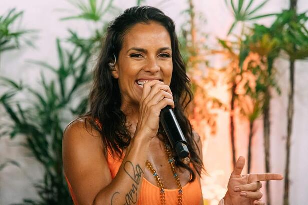 Ju Moraes de regata laranja, sorrindo, segurando um microfone de fio