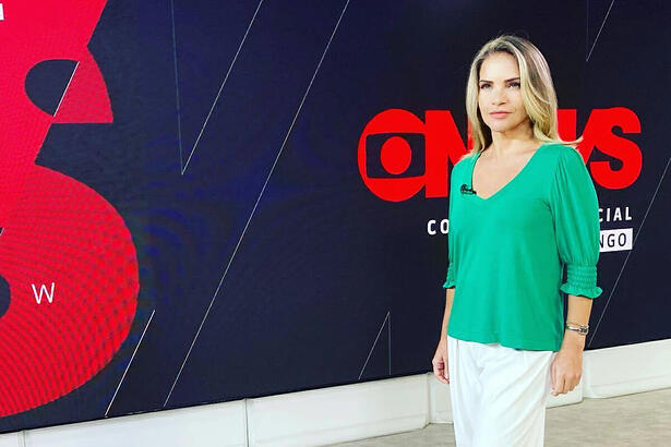 Leila de camisa verde e calça branca, na frente do telão nos bastidores