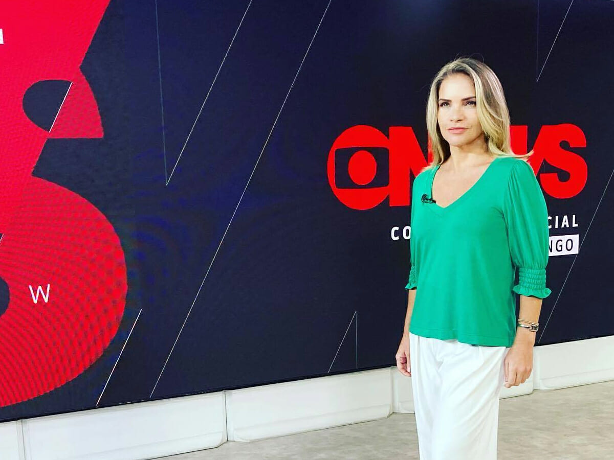 Leila de camisa verde e calça branca, na frente do telão nos bastidores