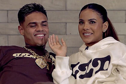MC Cabelinho e Bella Campos sentados em um sofá, em trecho da entrevista pata o Fantástico