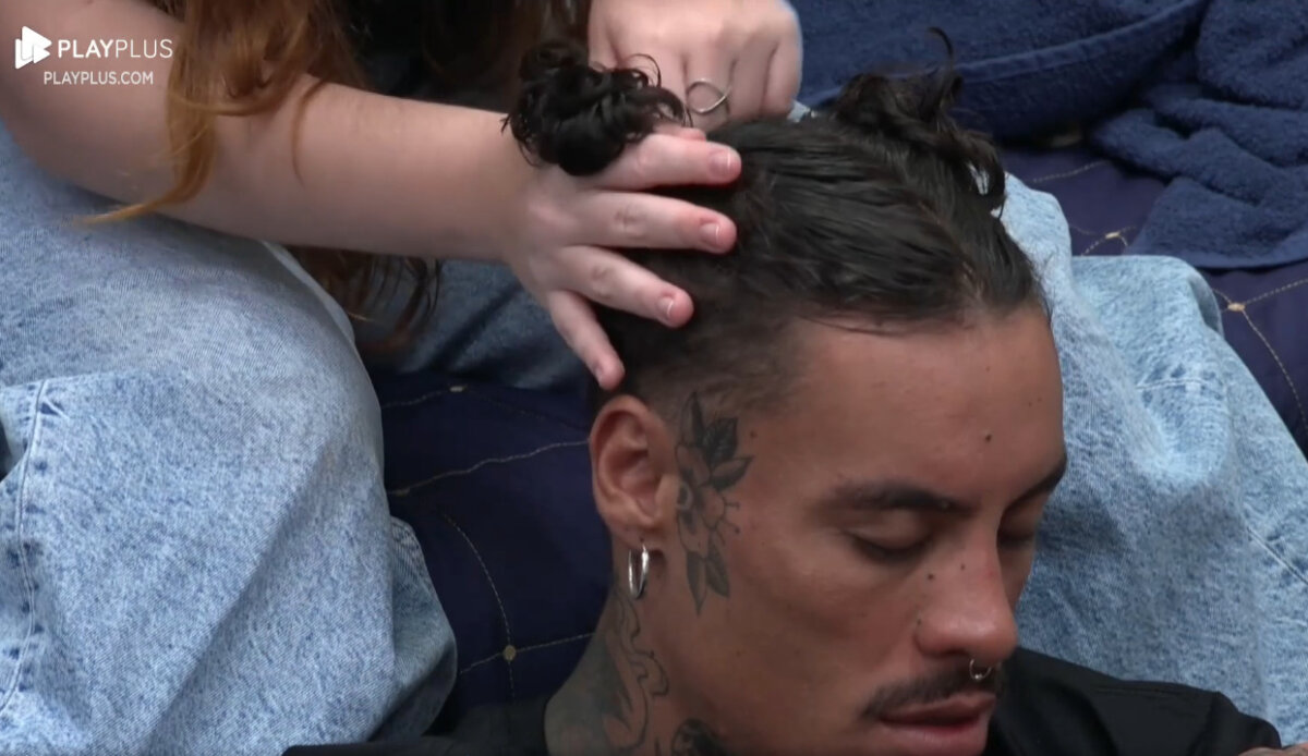Murilo Dias sentado, olhando pra baixo enquanto Giulia pentea seu cabelo