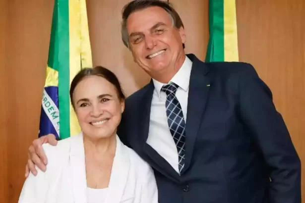 Regina Duarte de blazer branco, sorrindo, com cabelo preso ao lado de Bolsonaro, de paletó e gravata, sorrindo, no Palacio do Planalto