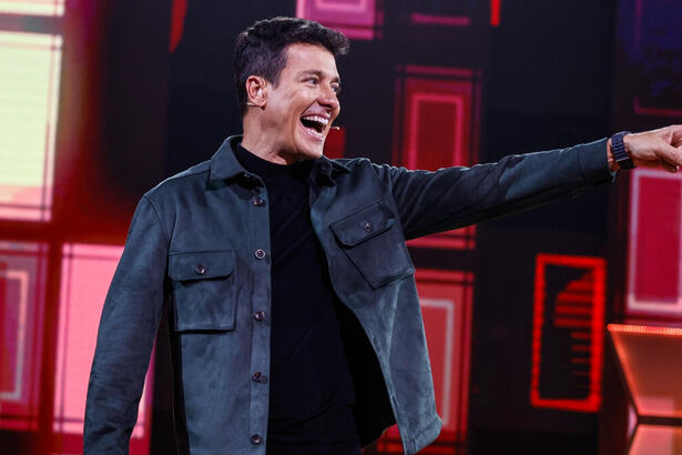 Rodrigo Faro sorrindo e apontando para o lado no palco do Canta Comigo 5