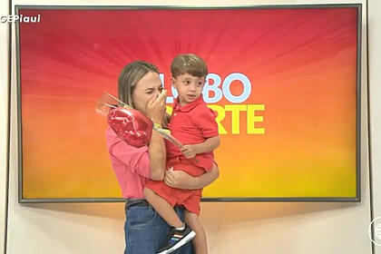Stephanie Pacheco, com o filho no colo e a mão no rosto emocionada, no estúdio do Globo Esporte PI