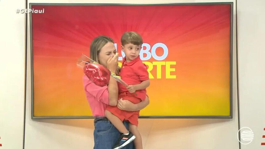 Stephanie Pacheco, com o filho no colo e a mão no rosto emocionada, no estúdio do Globo Esporte PI