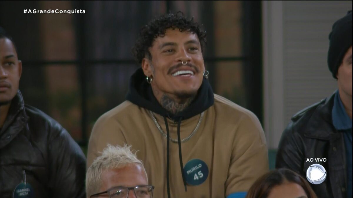Murilo de camisa bege, sorrindo, comemorando o resultado da votação de A Grande Conquista