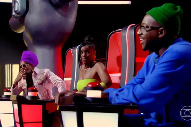 Carlinhos Brown, IZA e Mumuzinho sentados na cadeira de técnico do The Voicde Kids 8