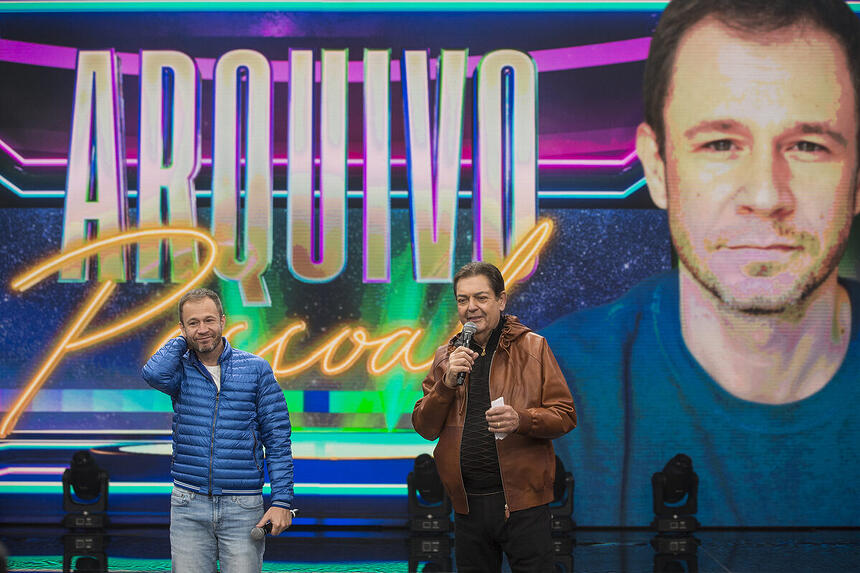 Tiago Leifert se emociona ao lado de Faustão no palco do Faustão na Band. Atrás deles estão o logo do Arquivo Pessoal