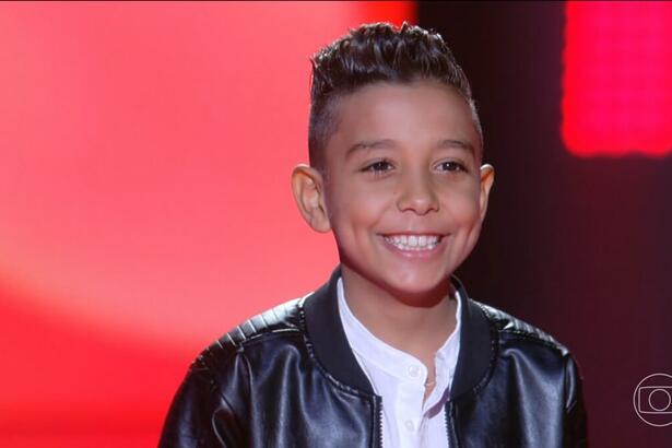 Marlysson Reis sorrindo no palco do The Voice Kids 8. Cantor mirim passa para a próxima etapa do programa