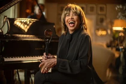 Tina Turner sorrindo sentada próximo ao piano