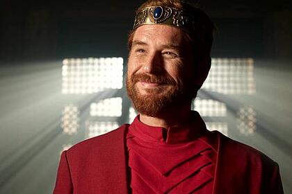 Rei Davi, Cirillo Luna, em cena da série Reis com uma vestimenta vermelha e uma coroa na cabeça
