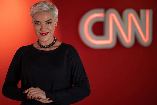 Fabíola Kassin no cenário da CNN Brasil com o logo do canal ao fundo