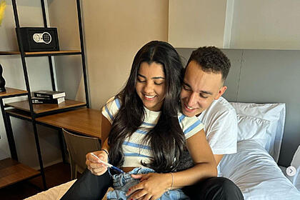 João Gomes abraça Mirelle que segura teste de gravidez na cama
