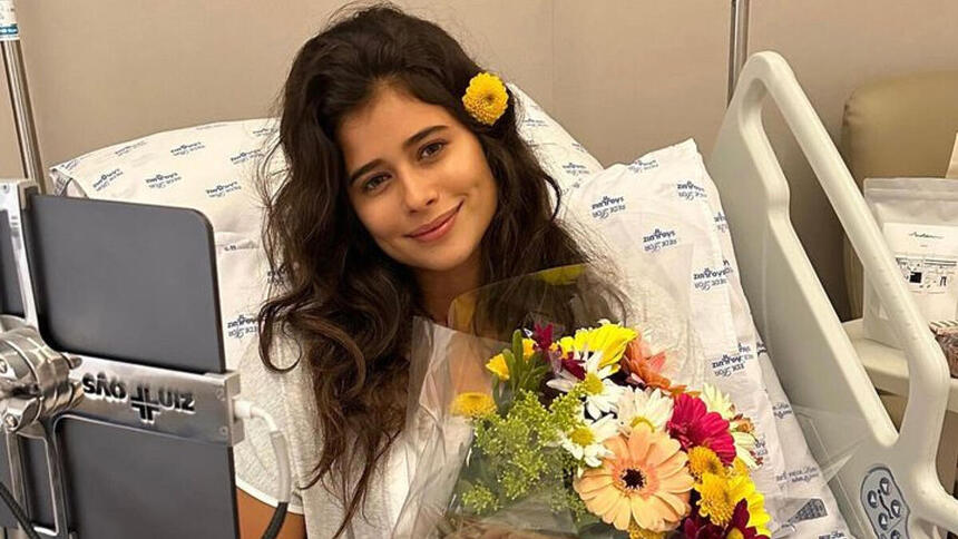 Isadora Cruz deitada em um leito de hospital com um flor por cima