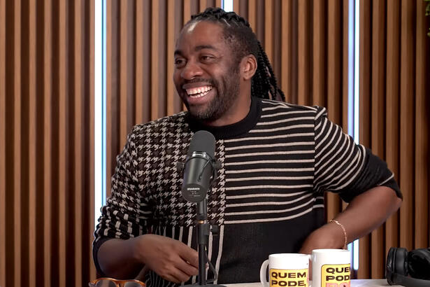 Lázaro Ramos sorrindo, sentado, durante entrevista para o Quem Pode Pod