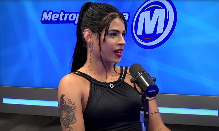 Sophia Narclay de camisa preta, cabelo preto preso, de lado, sentada durante entrevista