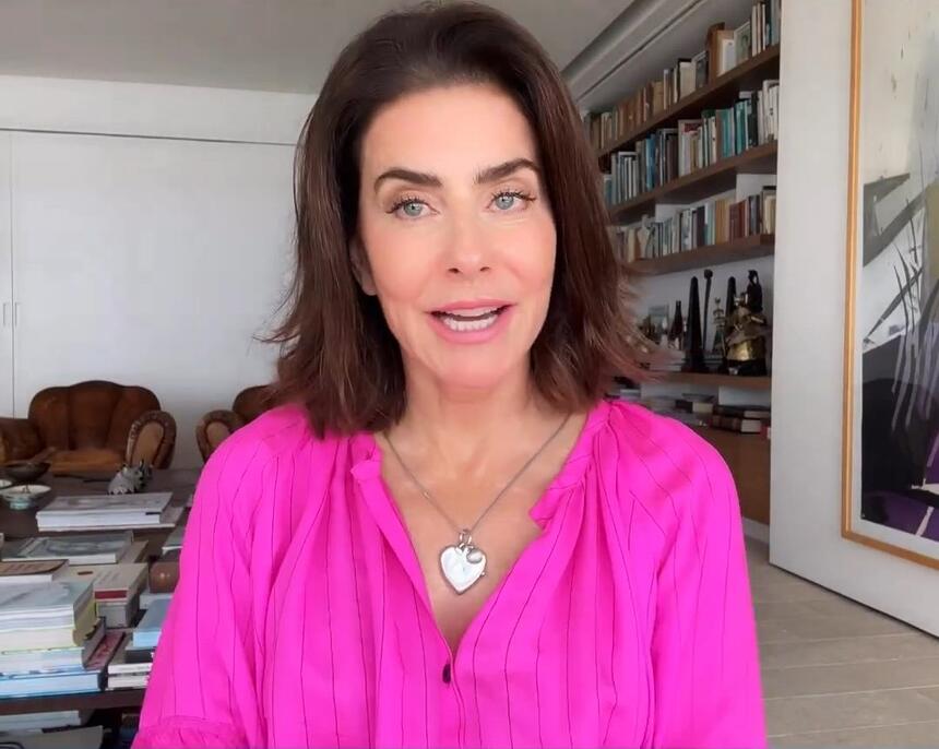 Maitê Proença de blusa rosa gravando vídeo em sua casa